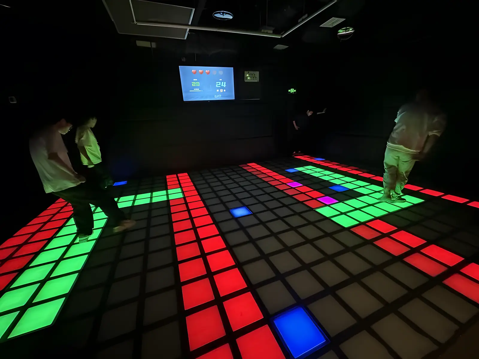 Players stepping along green paths between red lava tiles, with the scoreboard on the back wall
